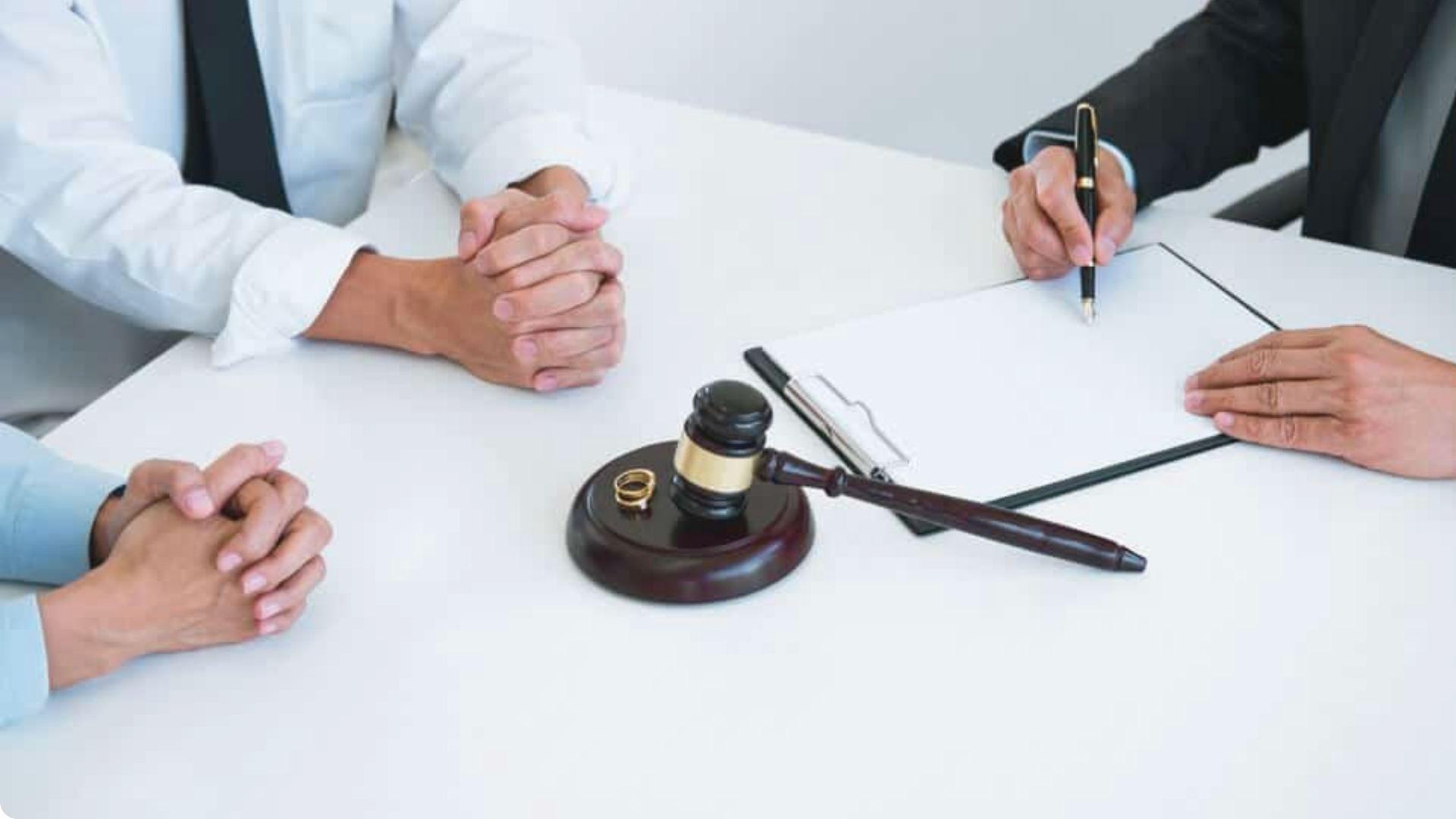 Couple at lawyer's table with wedding rings and gavel discussing divorce settlement