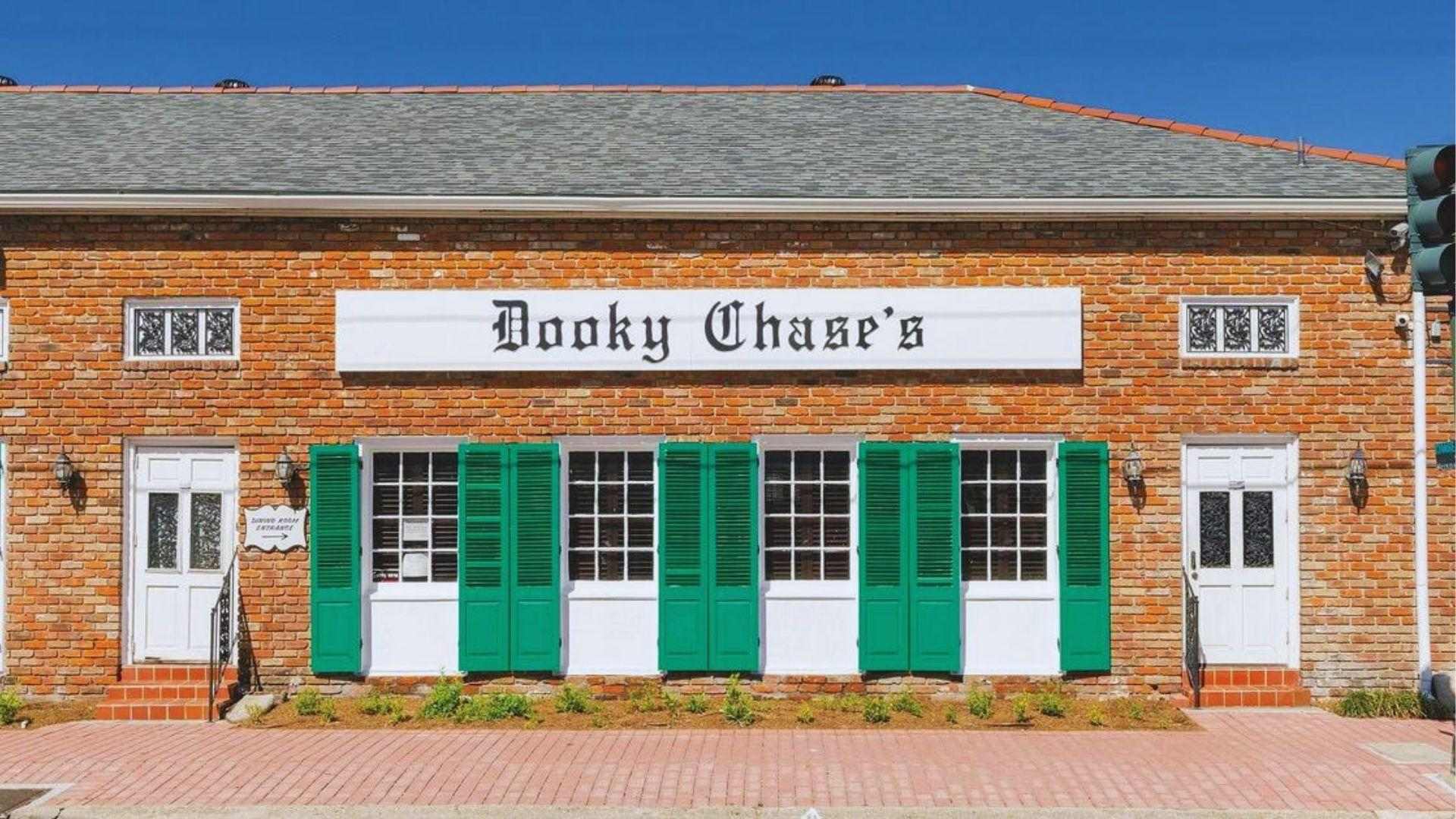 Exterior of Dooky Chase's restaurant with green shutters white sign and blue sky above sidewalk.