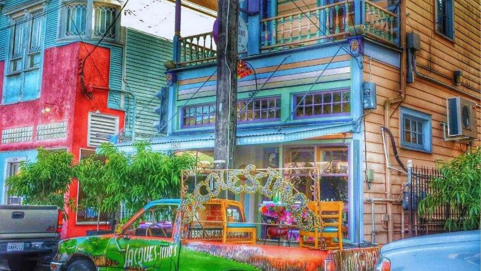 Vibrantly painted street corner with multicolor buildings and art-covered pickup truck displaying glittering carnival decorations.