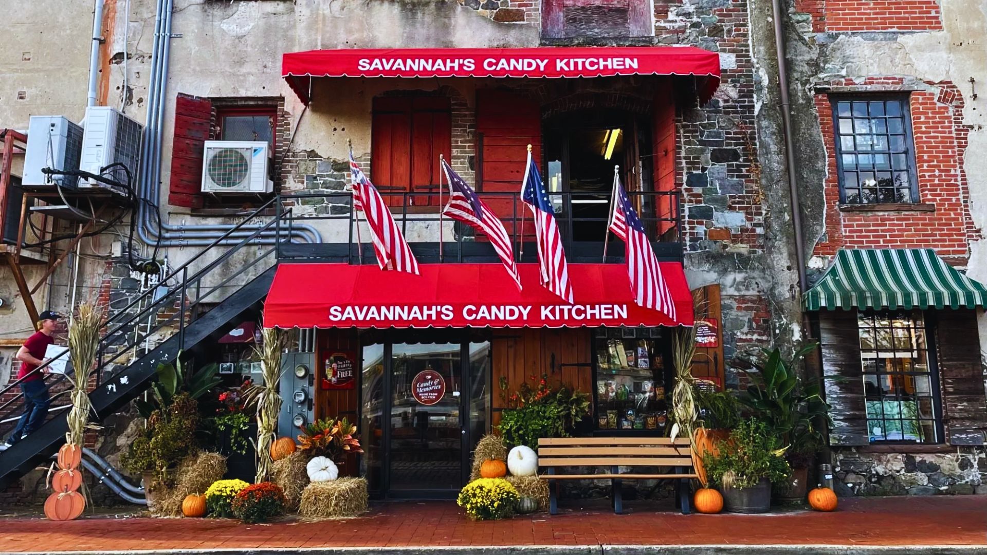 A storefront of Savannah's Candy Kitchen adorned with American flags, autumn pumpkins, and red awnings.
