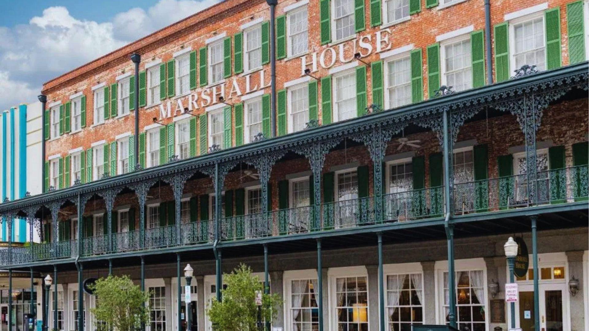 Red brick Marshall House hotel with green shutters and ornate ironwork balconies in downtown Savannah.