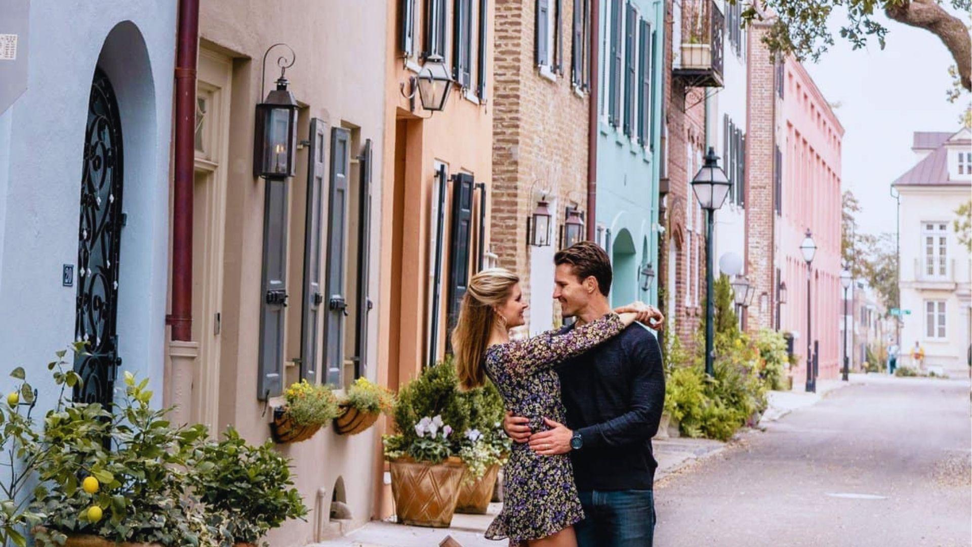 Romantic couple embracing on colorful Rainbow Row street with pastel historic houses and hanging lanterns.