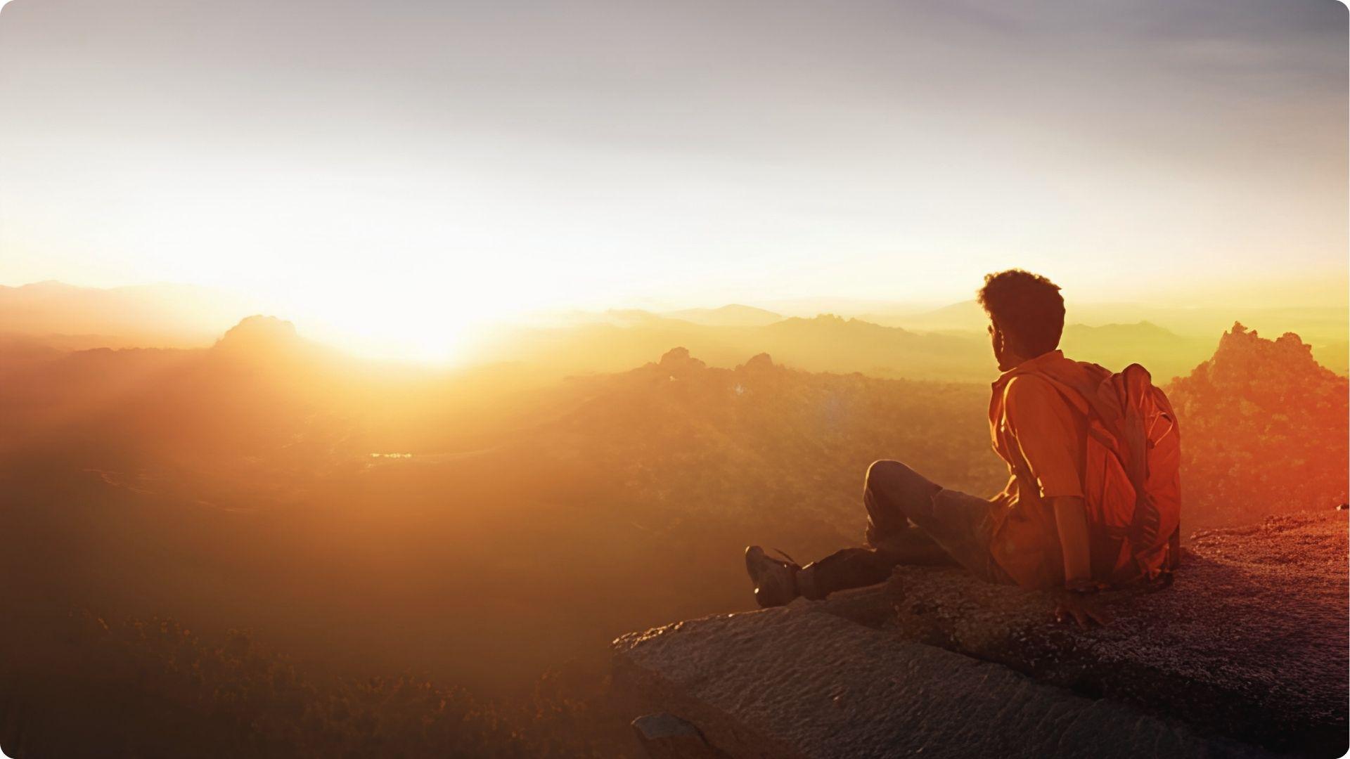 Hiker with backpack watching sunrise over valley from cliff near East Beach St Simons Island.