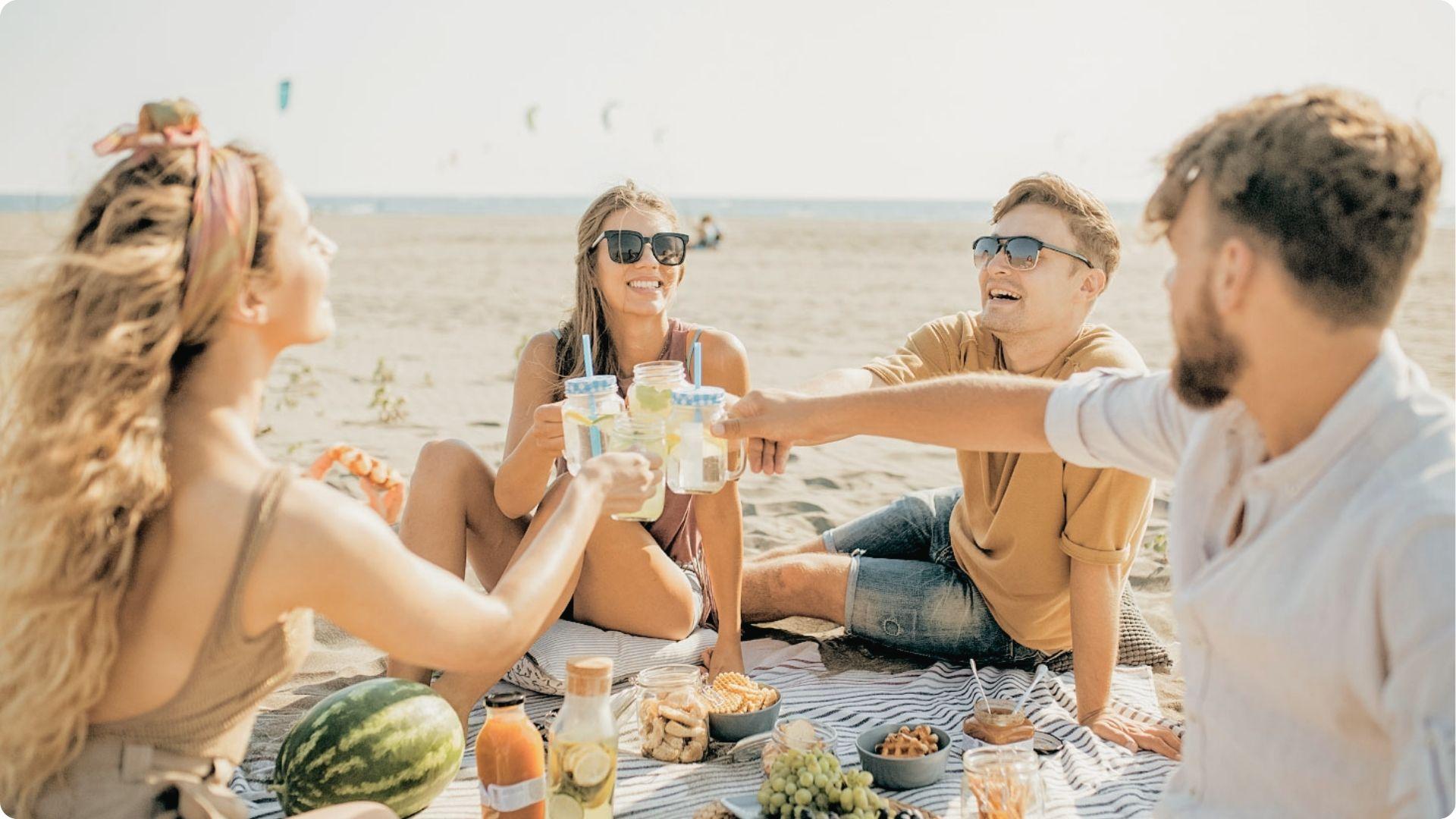 Friends cheering with drinks at beach picnic on East Beach St Simons with snacks and sunny ocean.