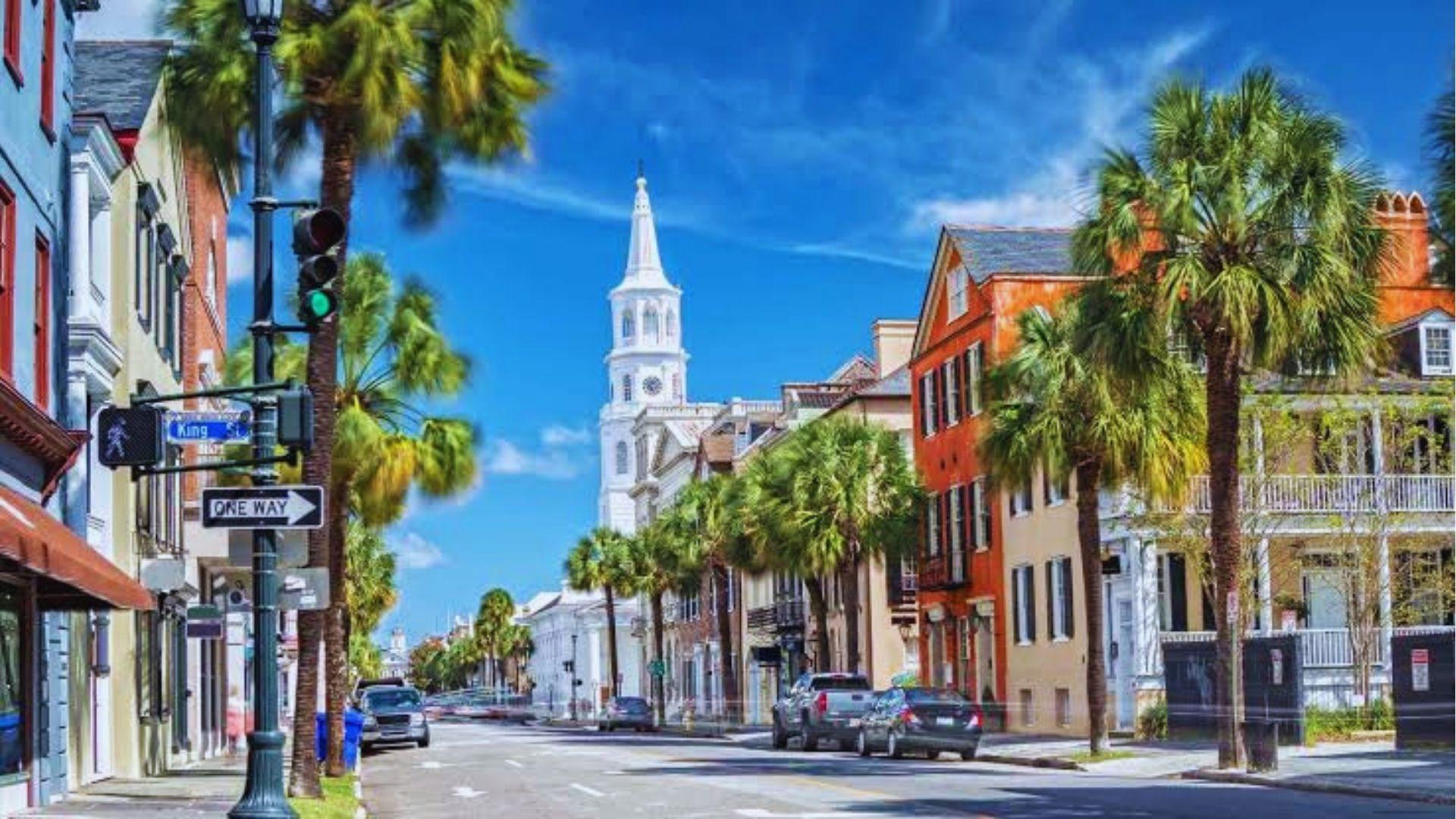 Sunny King Street Charleston with historic buildings palm trees white church steeple and street signs.