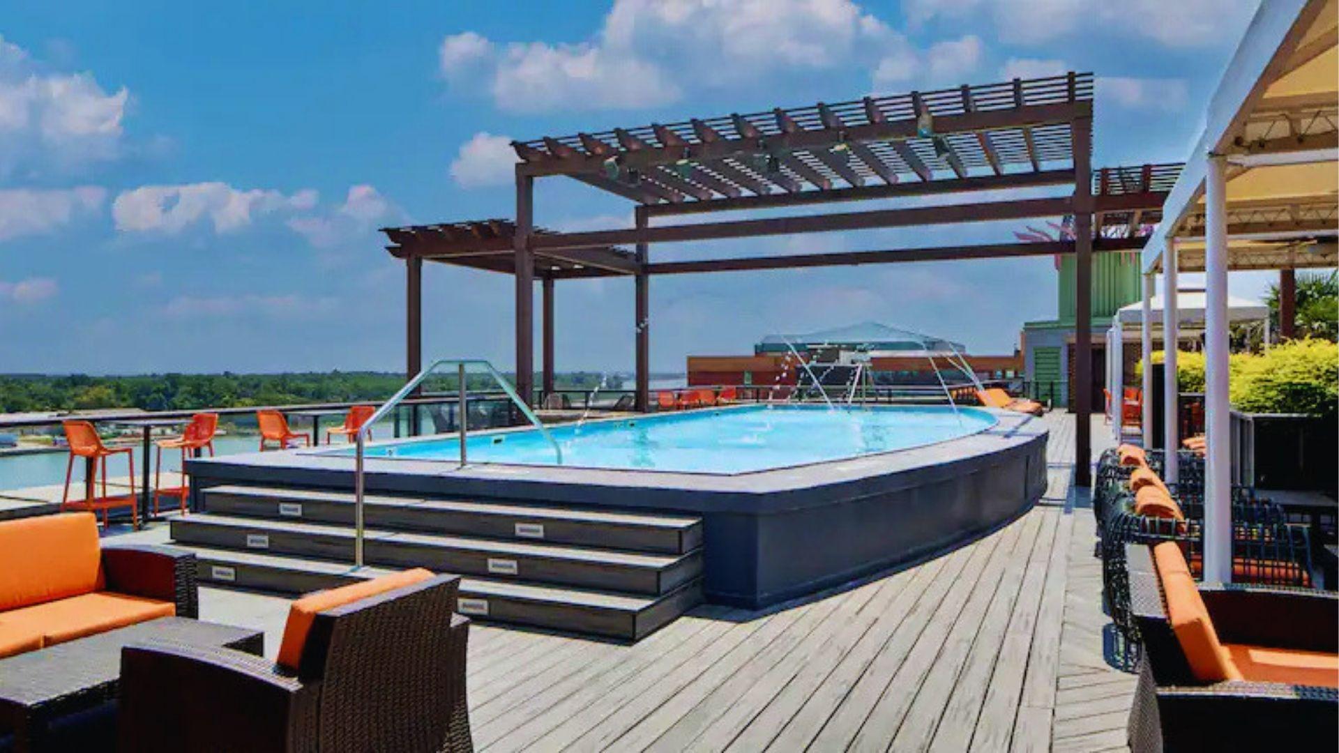 Pool deck with orange lounge chairs pergola and panoramic river view under bright blue sky.