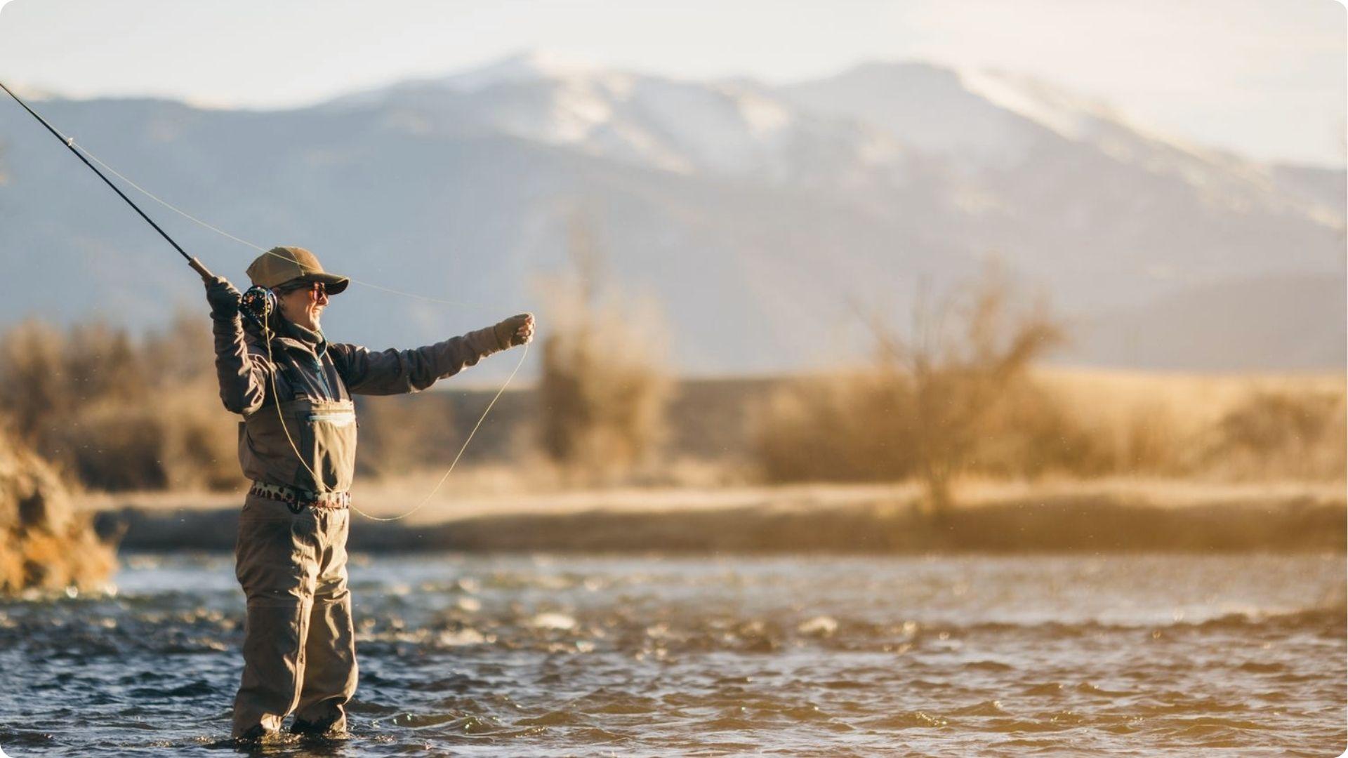 Woman fly fishing in the river near East Beach St Simons with mountains glowing in soft morning light.