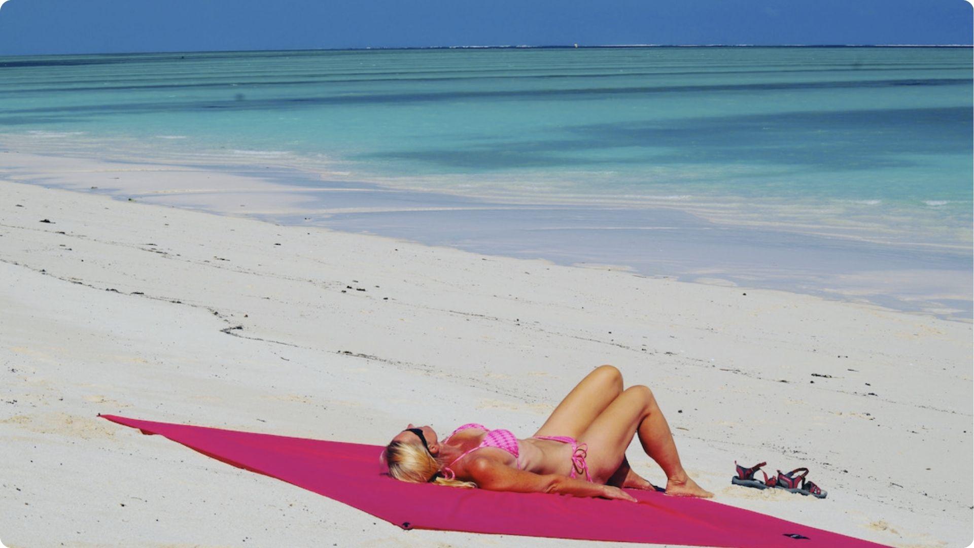 Woman relaxing on pink towel sunbathing at East Beach St Simons white sand and turquoise water.