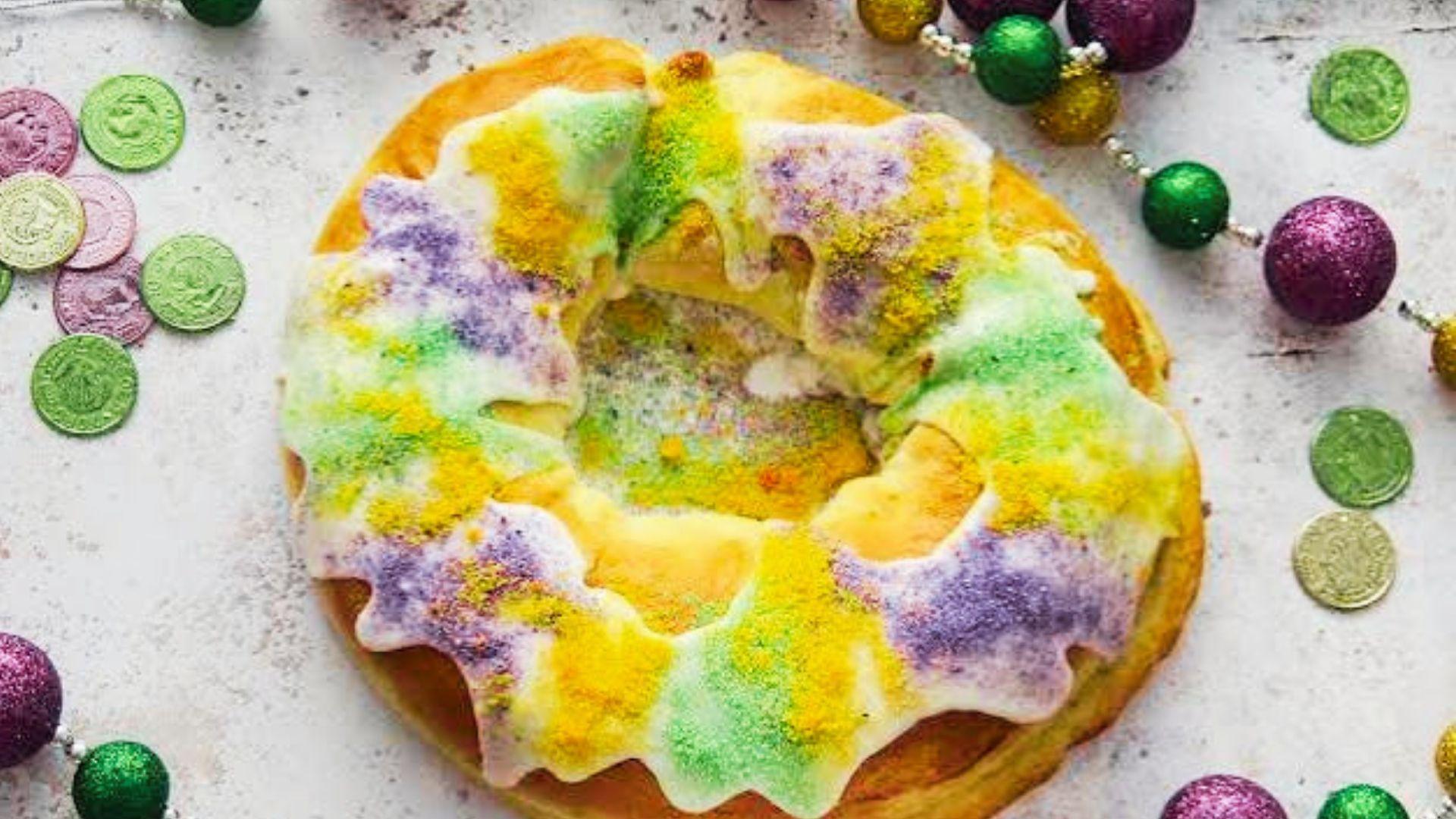 A ring-shaped king cake decorated with purple, gold, and green sugar crystals on a white platter.