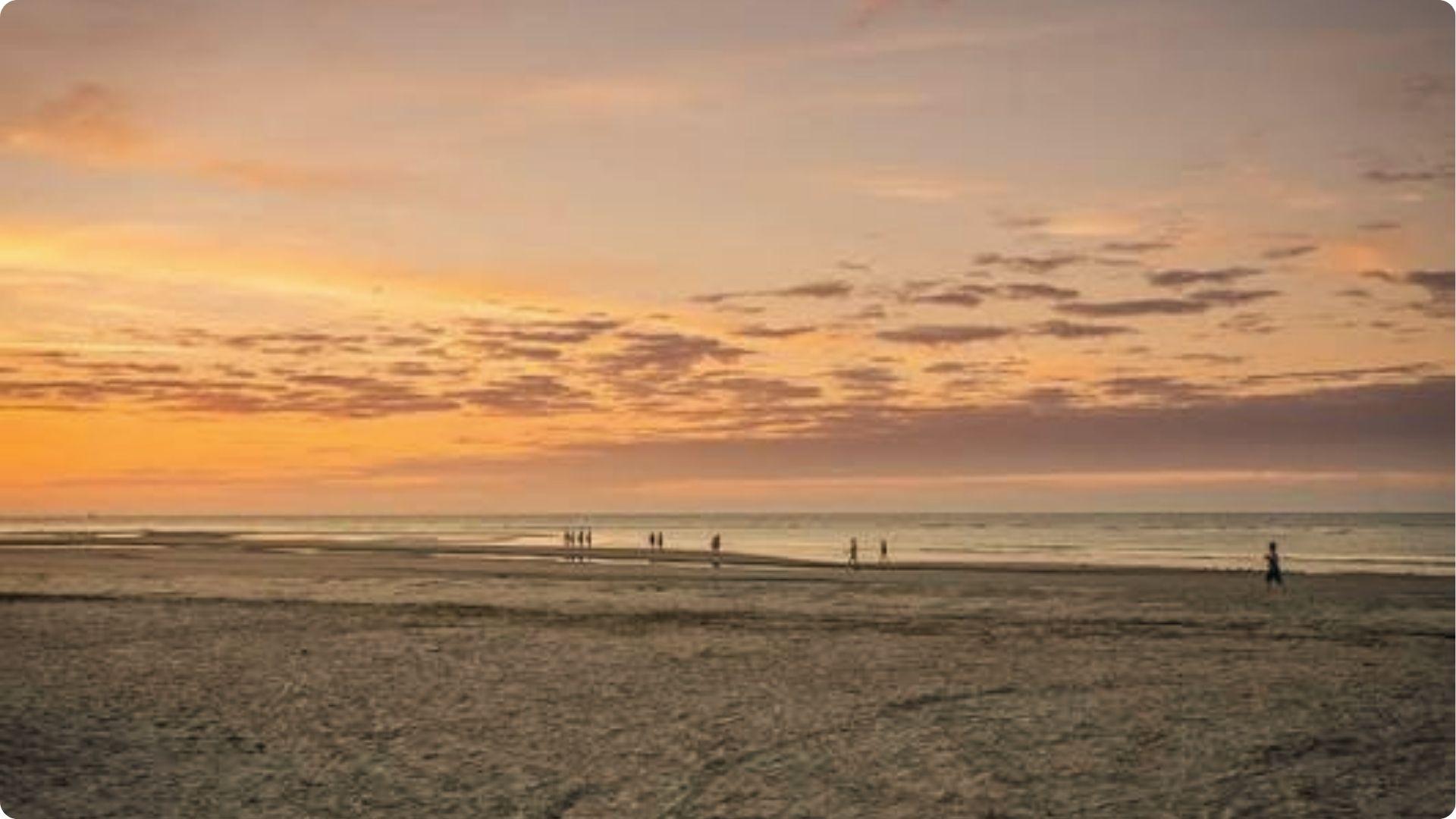 Silhouettes strolling on wet sand during sunset at East Beach St Simons under an orange cloudy sky.