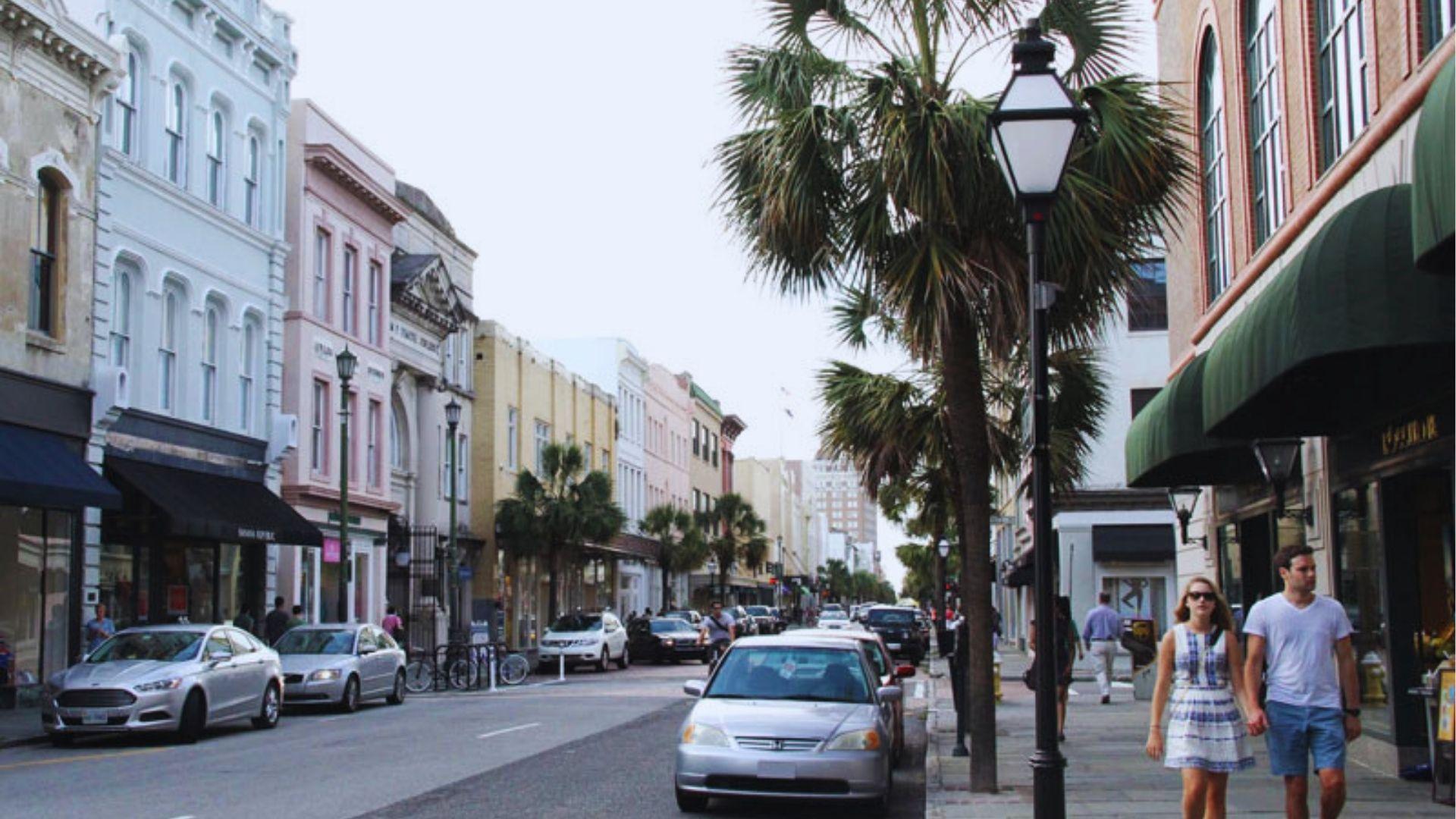 Couple strolling hand-in-hand on King Street Charleston with historic buildings, palm trees and storefront awnings.