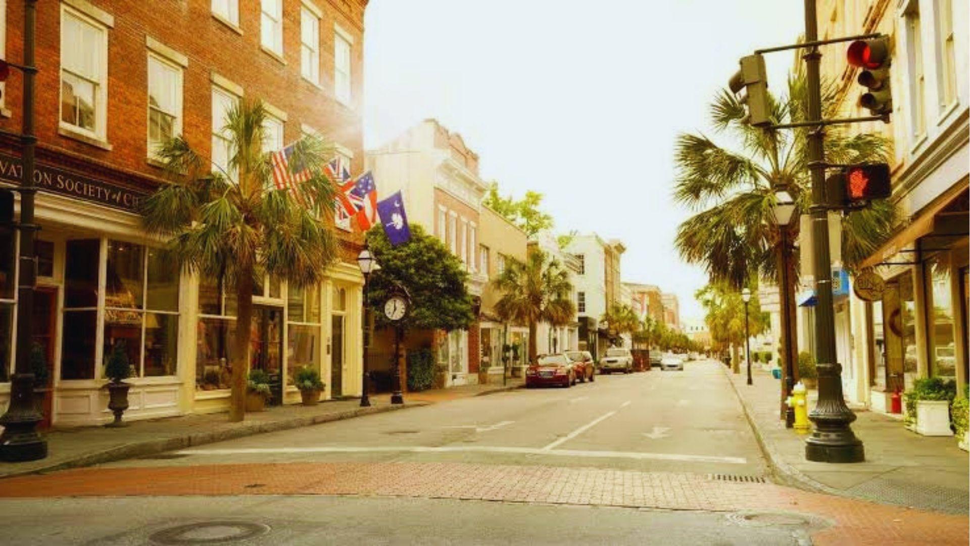Historic Charleston street with brick storefronts, American flags palm trees and glowing afternoon sunlight overhead.