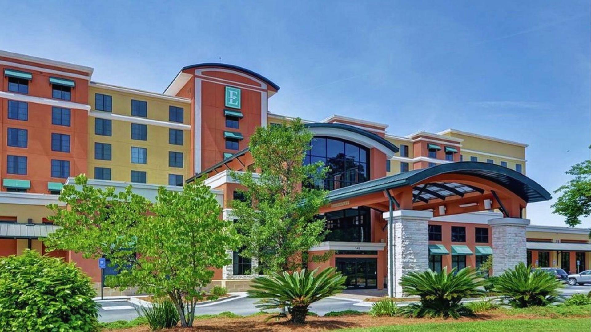 Embassy Suites hotel exterior with covered stone entrance palm plants and landscaping under blue sky.