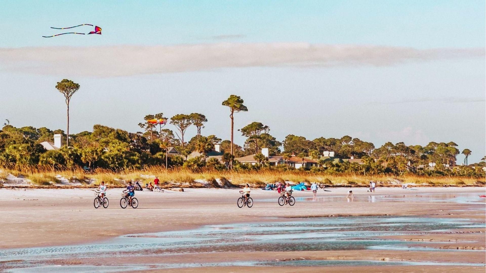 Bicycles on wet sandy beaches with colorful kites flying above pine trees and beach houses.