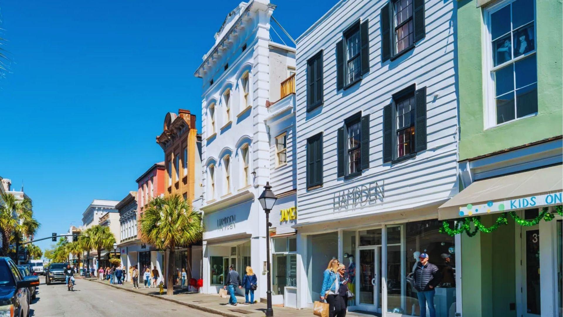 Shoppers walking past Hampden boutique storefronts on King Street Charleston with palm trees and buildings.