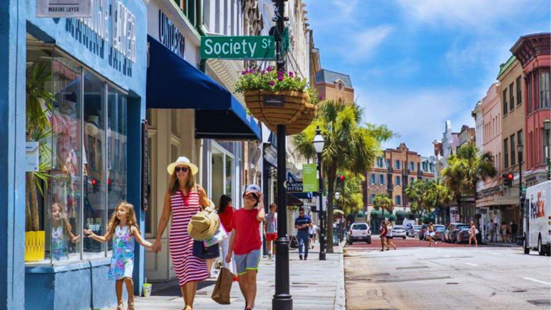 Mother and children shopping on Society Street Charleston with storefronts, palm trees and flower baskets.