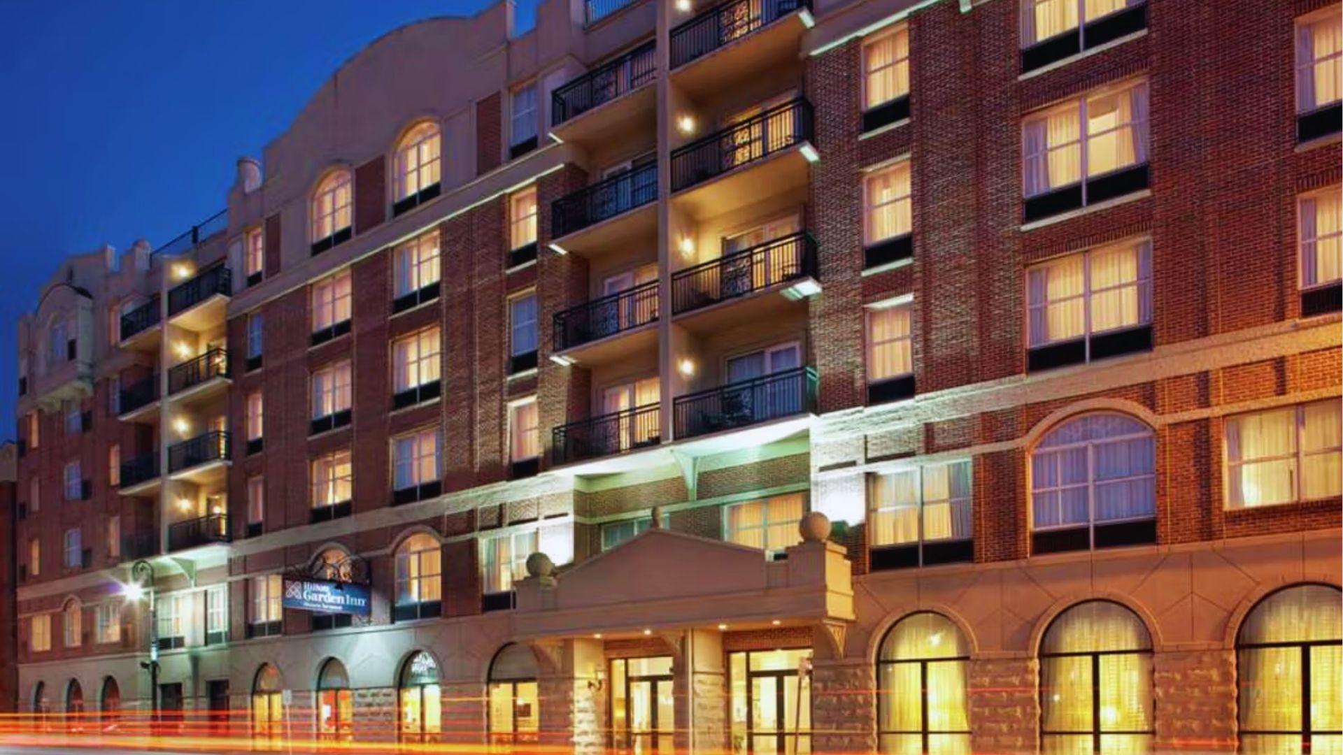 Hilton Garden Inn brick hotel at dusk with illuminated balconies, arched windows and glowing lights.