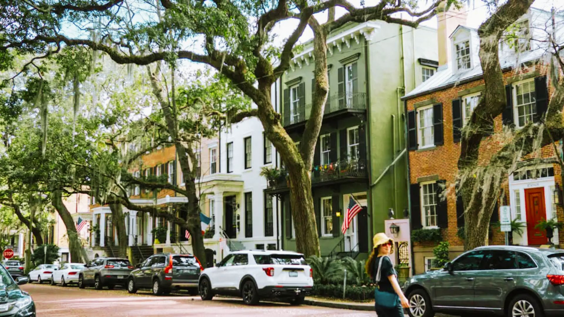 Tourist walking past colorful historic homes under mossy oak trees in Savannah